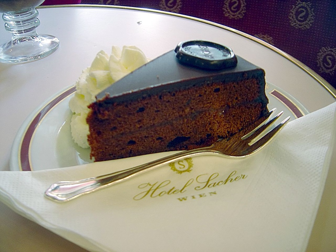 En elegant chokladkaka på en fin porslinstallrik med logotypen 'Hotel Sacher Wien', vilket representerar en lyxig matupplevelse på hotell.