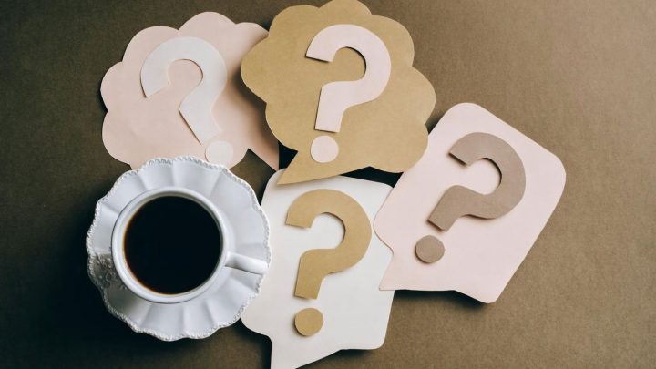 Kaffekopp omgiven av tankebubblor med frågetecken, symboliserar ekonomiska frågor.